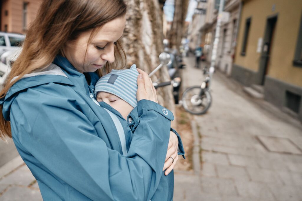 Mamalila Shelter Babywearing Rain Jacket lifestyle image, woman carrying baby on her front