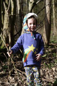 Child wearing Piccalilly rainbow applique sweatshirt and Flapper hat standing in the woods