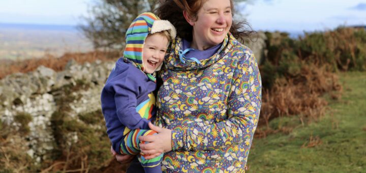 Woman holding child outside, both wearing Piccalilly Rainbow Cosmic Weather collection