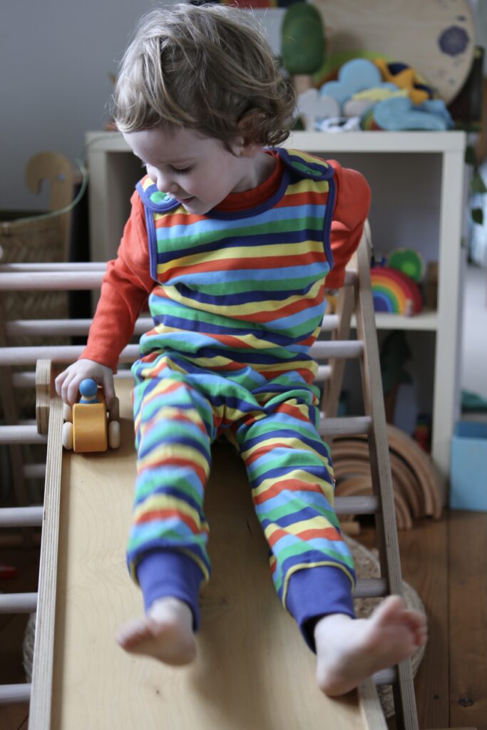 Child wearing Piccalilly Rainbow Stripe dungarees on a Triclimb pikler triangle